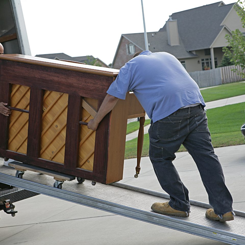 Movers using a dolly and straps to move a heavy appliance